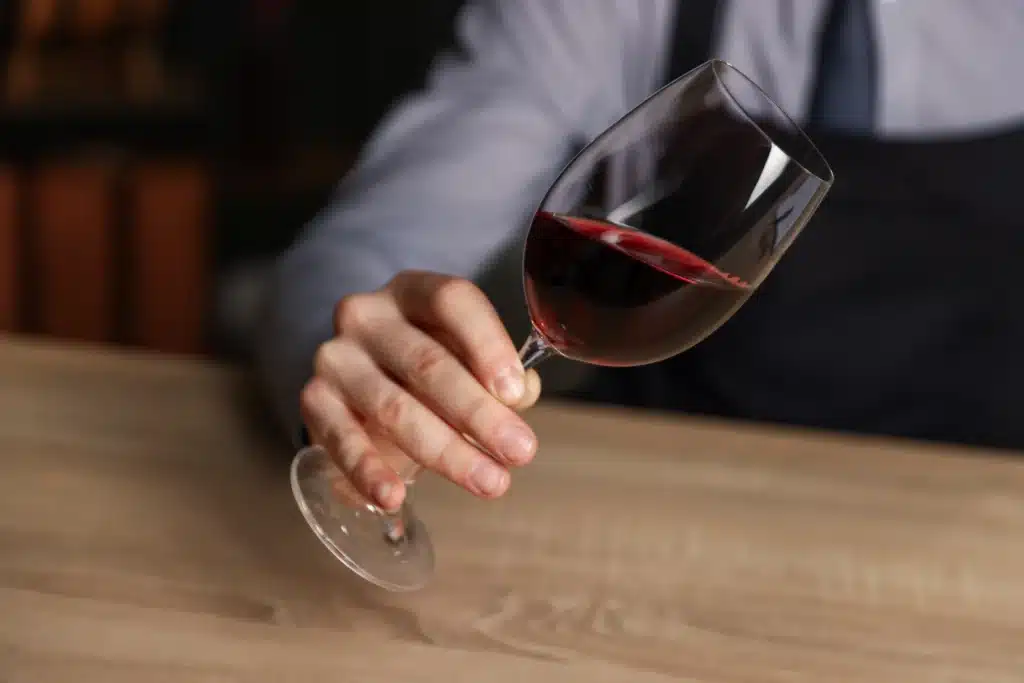 Dégustation de vin rouge par un sommelier professionnel Main de sommelier tenant un verre de vin rouge incliné sur une table en bois.